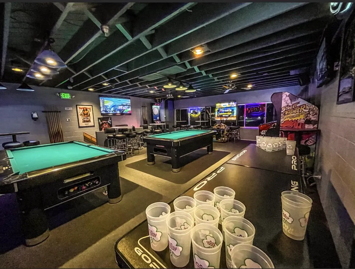 The games floor at The Blue Moon Lounge - two pool tables, a Pong PRO beer-pong table set up with cups, and a dartboard on the back wall