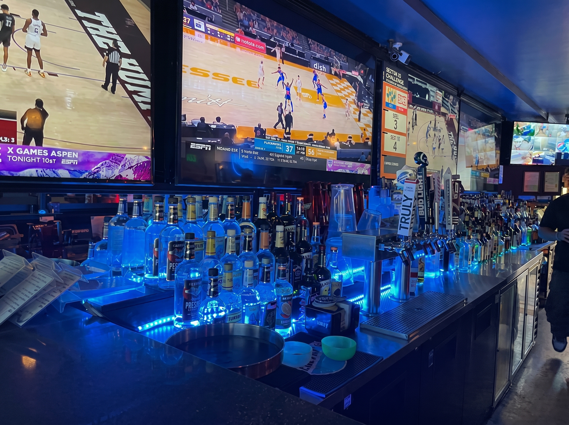 The back bar at The Blue Moon Lounge - full liquor lineup under blue light, games on every screen